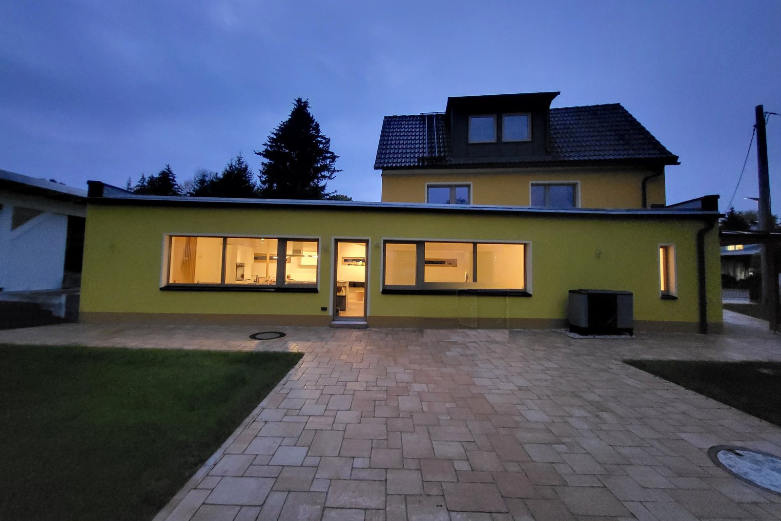 Große gepflasterte Terrasse vor dem Haus am Abend, die Fenster sind erleuchtet